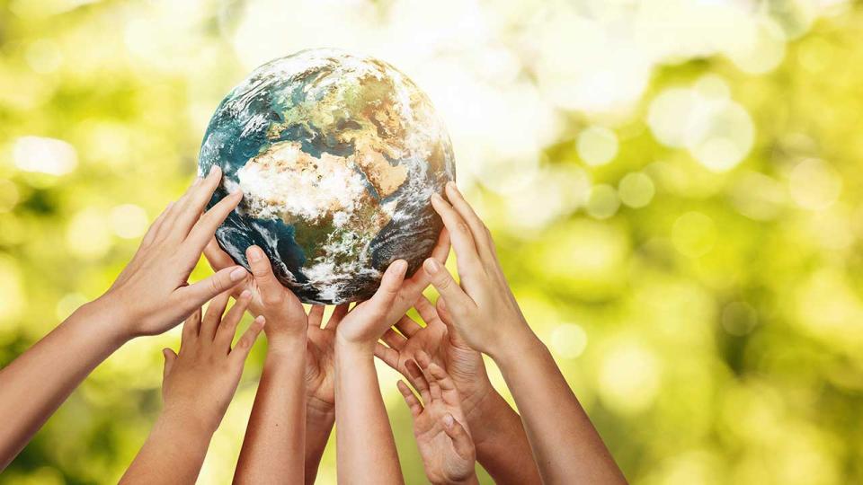 Gruppe von Kindern, die den Planeten Erde über einem unscharfen Naturhintergrund halten