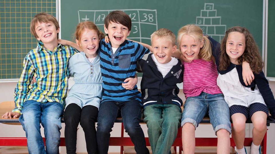 Mehrere Kinder sitzen auf einem Pult vor einer beschriebenen Tafel