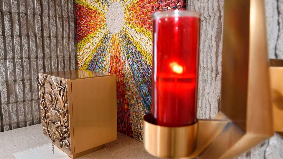 Rote Altarraumlampe oder Ewige Flamme am Tabernakel mit bronzenem Lamm Gottes Basrelief am Seitenaltar mit Sonnenmosaik in einer katholischen Kirche